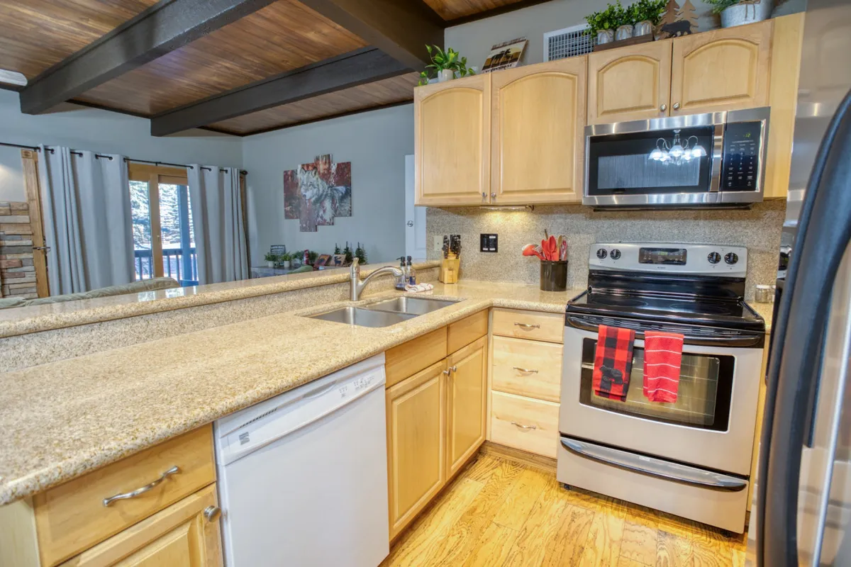 This image showcases a spacious kitchen featuring a granite countertop, sleek stainless steel appliances, and an open layout accentuated by rustic wooden beams. There are inviting spaces for cooking and gathering, and the breakfast bar clearly serves as a focal point for both meal preparation and casual conversation. The warm, welcoming atmosphere encourages socializing and easy entertaining.