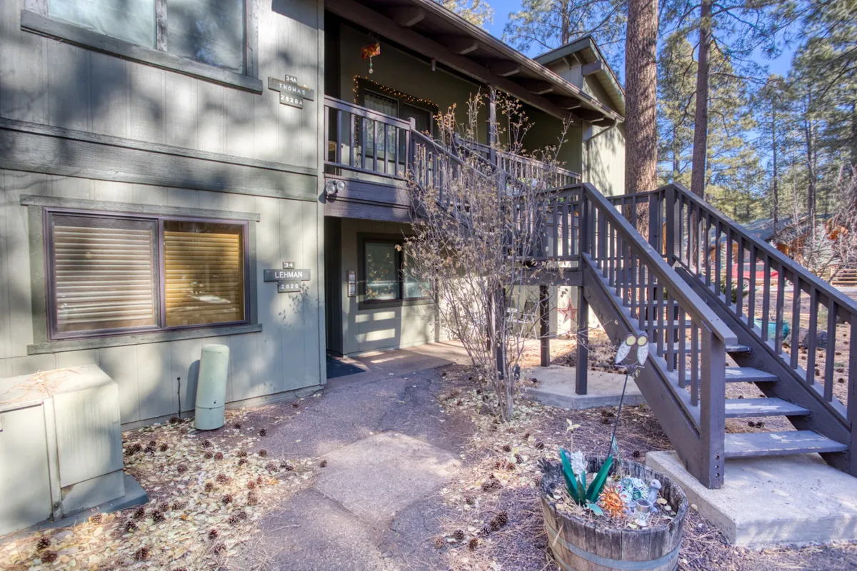 The hero image shows the welcoming exterior of a ground-floor condo in Pinetop Lakes Country Club, with a charming front staircase leading to the inviting front door, accented by a colorful flower pot. The peaceful setting hints at opportunities to enjoy nature, sip morning coffee on the porch, or take evening strolls under the stars.