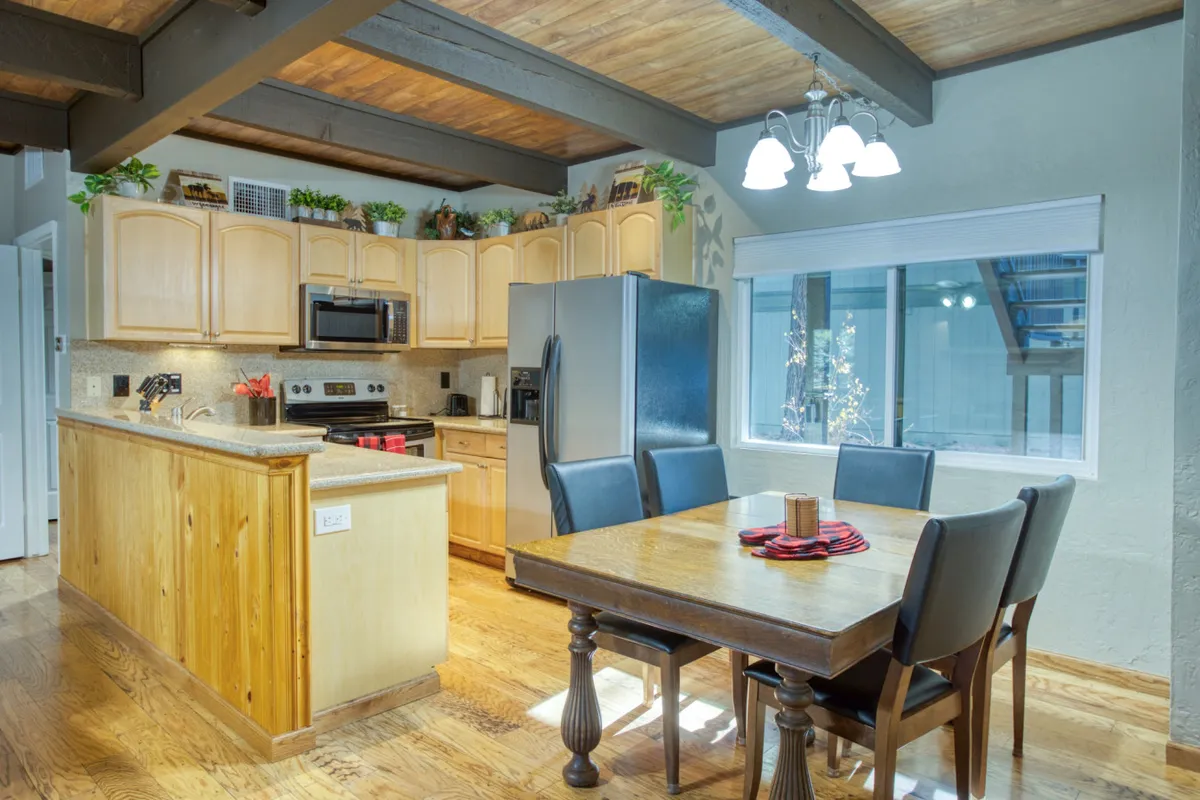 The dining area is the centerpiece here, with a dining table adjacent to a kitchen island and a window offering a scenic view. The cozy, welcoming ambiance is accentuated by soft lighting and homey touches. The scene hints at both celebratory meals and peaceful mornings, reinforcing the area’s versatility for family traditions and social gatherings.