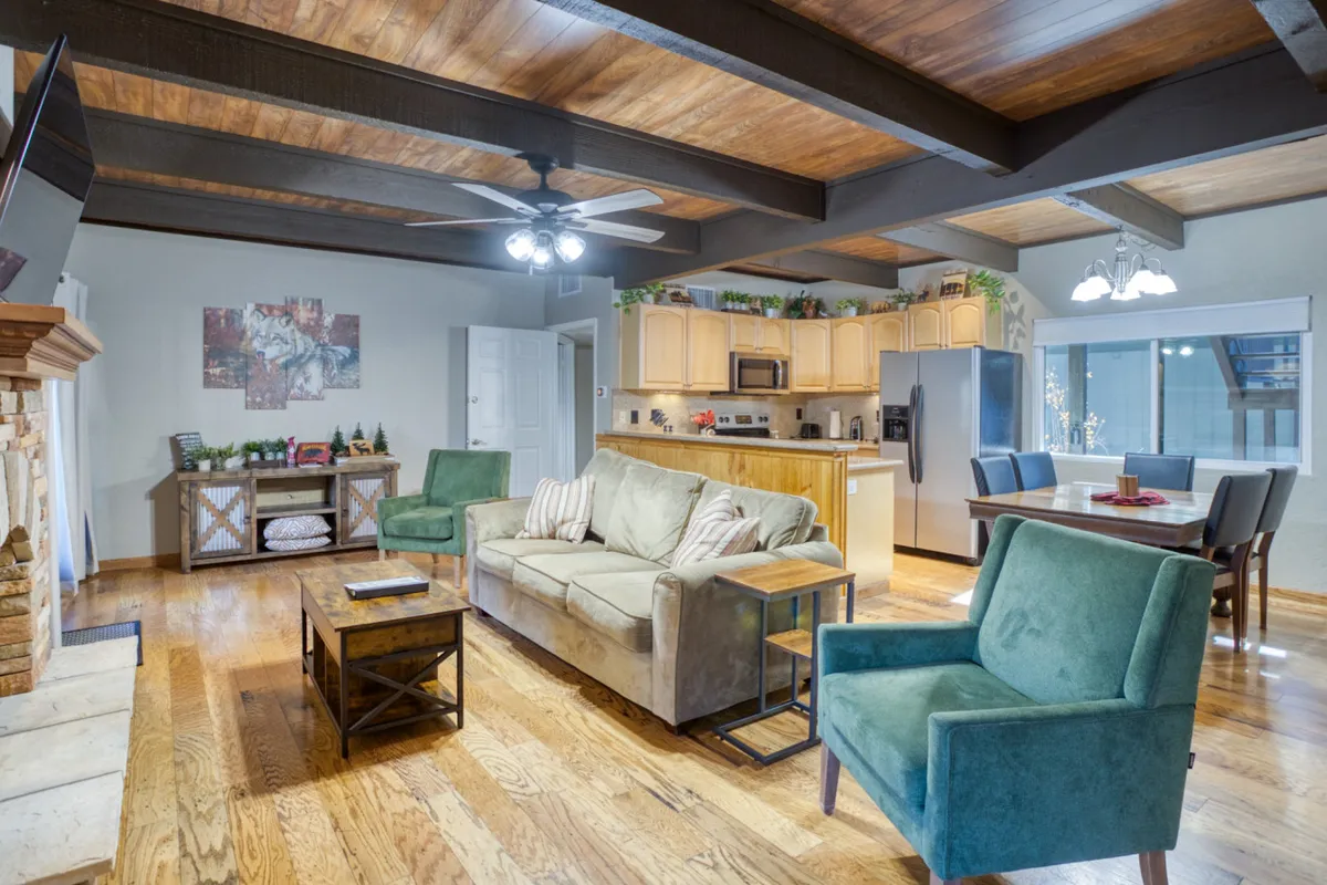 This open-concept interior shot seamlessly combines the living area, dining table, and a kitchen island. The fireplace is visible, reinforcing the central hearth theme. The space conveys a sense of togetherness, with comfortable furnishings arranged for group gatherings, dining, and entertaining. The cozy and inviting mood is evident, hinting at family meals and joyful moments shared in a well-lit, spacious environment.