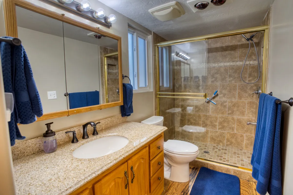 A beautifully appointed kitchen area with a granite countertop, large mirror, glass shower enclosure, and wooden cabinetry. The space is organized and inviting, reflecting thoughtful design and ample storage. Although the image includes a mirror and a shower, the granite countertop and cabinetry are also prominent, reinforcing the kitchen’s luxury and functionality.